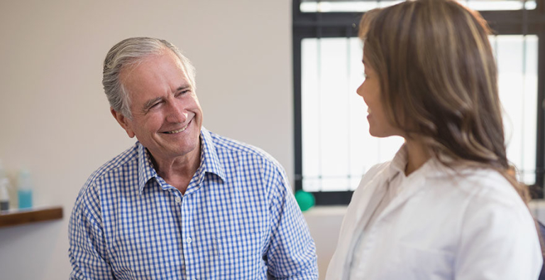 Smiling senior male patient in friendly conversation with female doctor during appointment