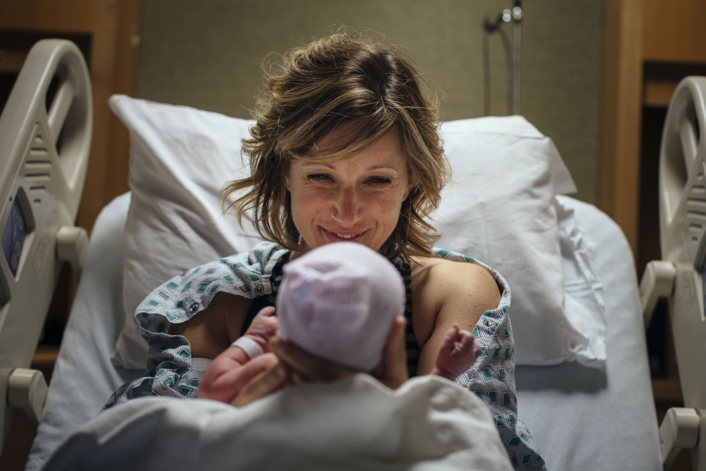 Woman smiling at her newborn baby in a hospital bed.