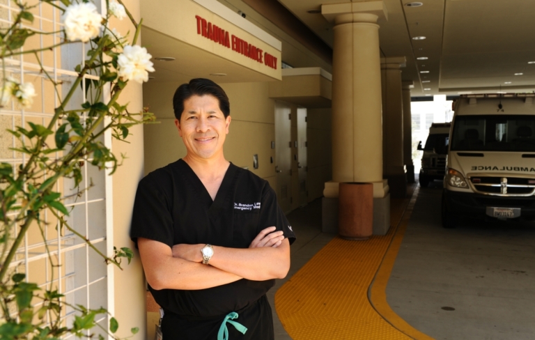 Emergency medicine physician standing confidently outside hospital trauma entrance with ambulance