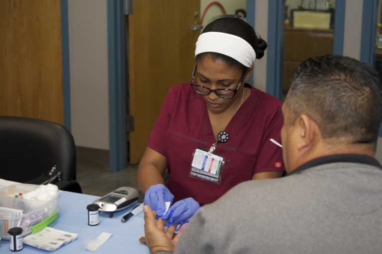 Nurse performing blood glucose finger stick test on male patient at clinic