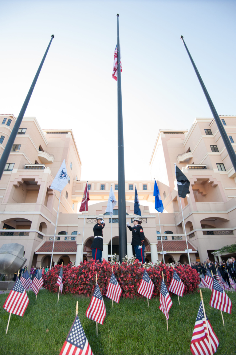 Military honor guard raising American flag at Huntington Hospital Veterans Day ceremony surrounded by American flags
