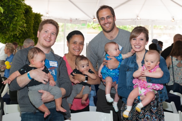 NICU reunion event with smiling parents holding their healthy babies under tent