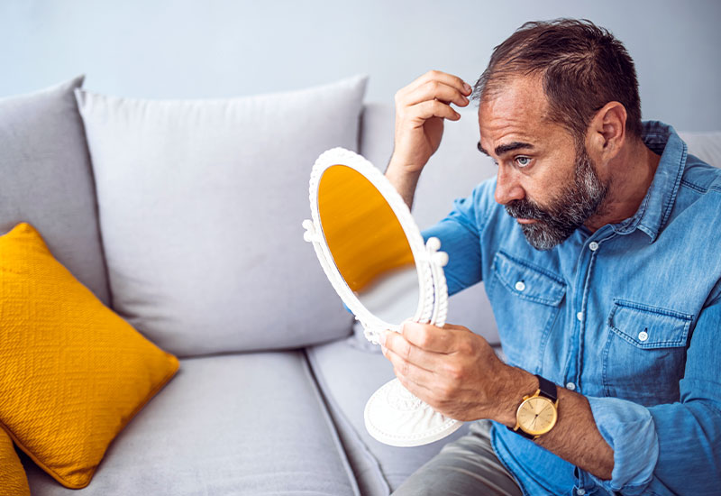 Senior man, looking in a mirror, and touching his hair
