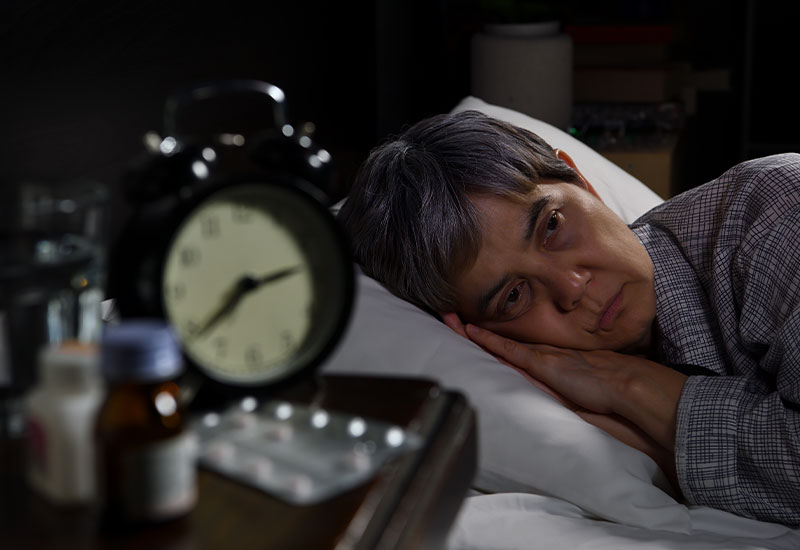 Senior woman, laying in bed in frustration, with alarm clock in the foreground